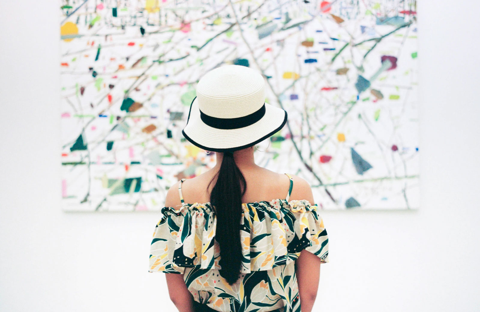 woman in a dress and hat looking at a painting