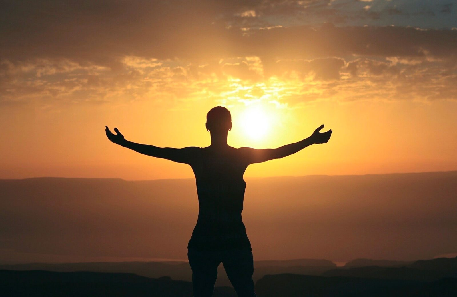 person with arms widely stretched facing the sunset