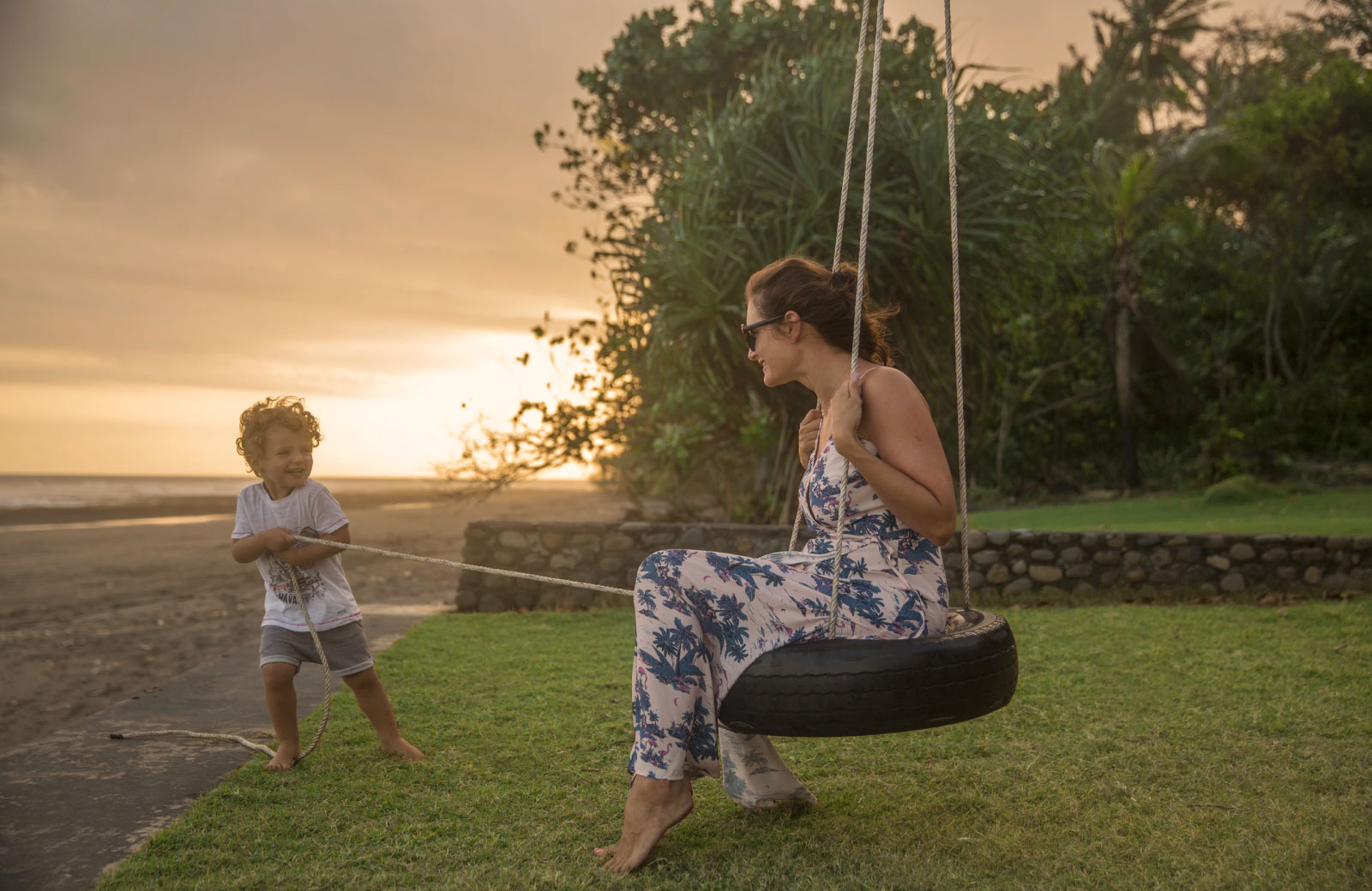 woman and boy playing in a swing by the beach