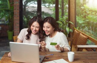 Two woman shopping on a laptop, one holding a credit card.