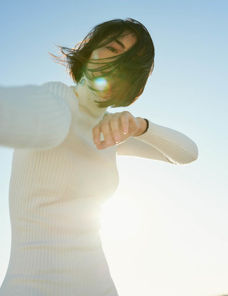 A woman in strikes a dance pose against a bright blue sky
