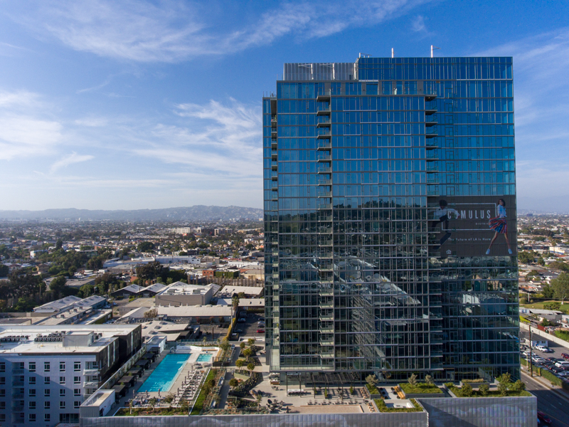 ARQ Residences — View of ARQ towering above amenity deck with pool and courtyards, with view of Culver City and Hollywood Hills in the background.
