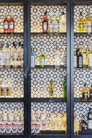 Lit shelves of alcohol bottles behind glass doors against a geometric tile wall.