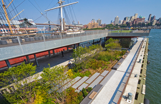 View of Pier 15 park from the East River Esplanade with large ship docked in the background.