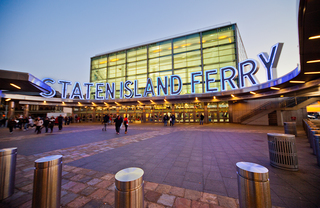 The entry courtyard of the Staten Island Ferry terminal at dusk, with people walking in and out.