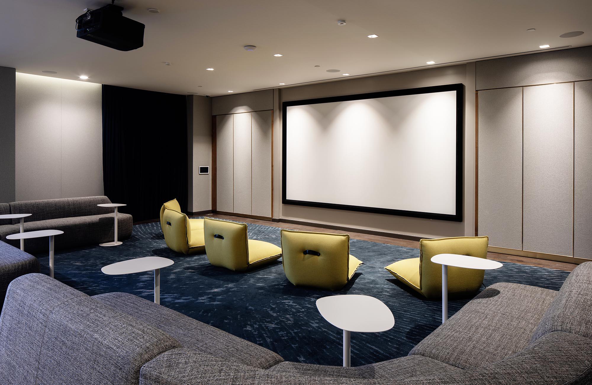 Spacious screening room with expansive lounge seating and cocktail tables, as well as floor loungers