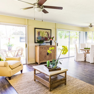 A living room with a yellow armchair, jute area rug on dark hardwood floors and a ceiling fan, adjacent to the patio