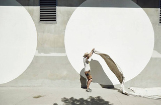 A painter laying a drop cloth on a sidewalk to paint a wall mural