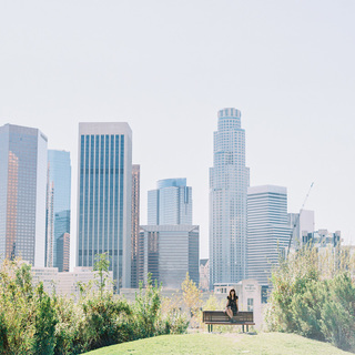 A woman sitting on a park bench with skyscrapers in the backdrop