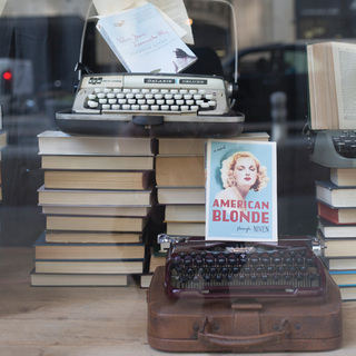A retail window display with stacks of books and two vintage typewriters