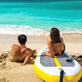 A woman lounging on a paddle board next to a man lounging on the sand, gazing out at the water