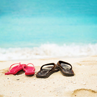 Red flip flops and black flip flops in the sand on the beach