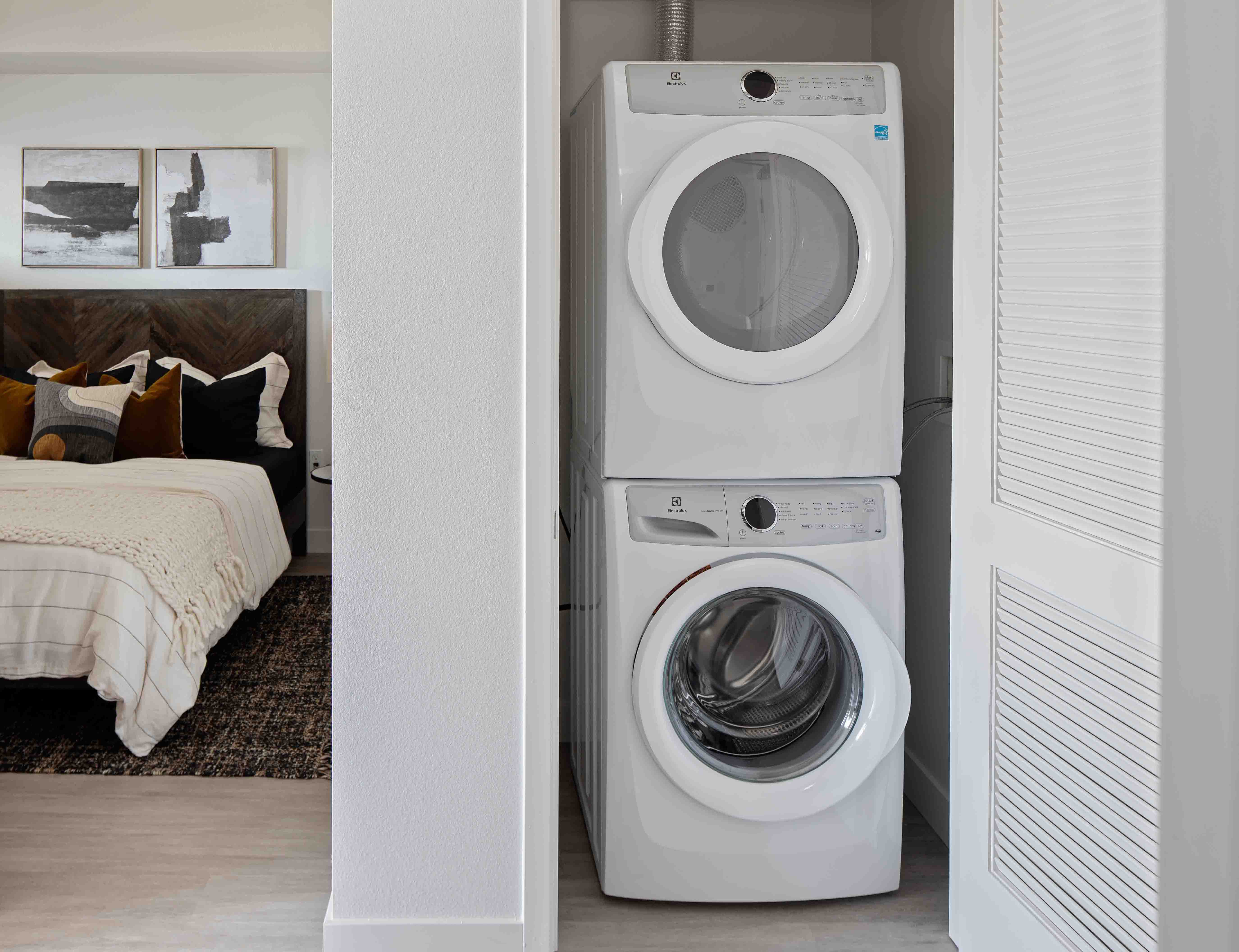 Stacked front-loading Electrolux washer and dryer tucked into a laundry closet near the bedroom.