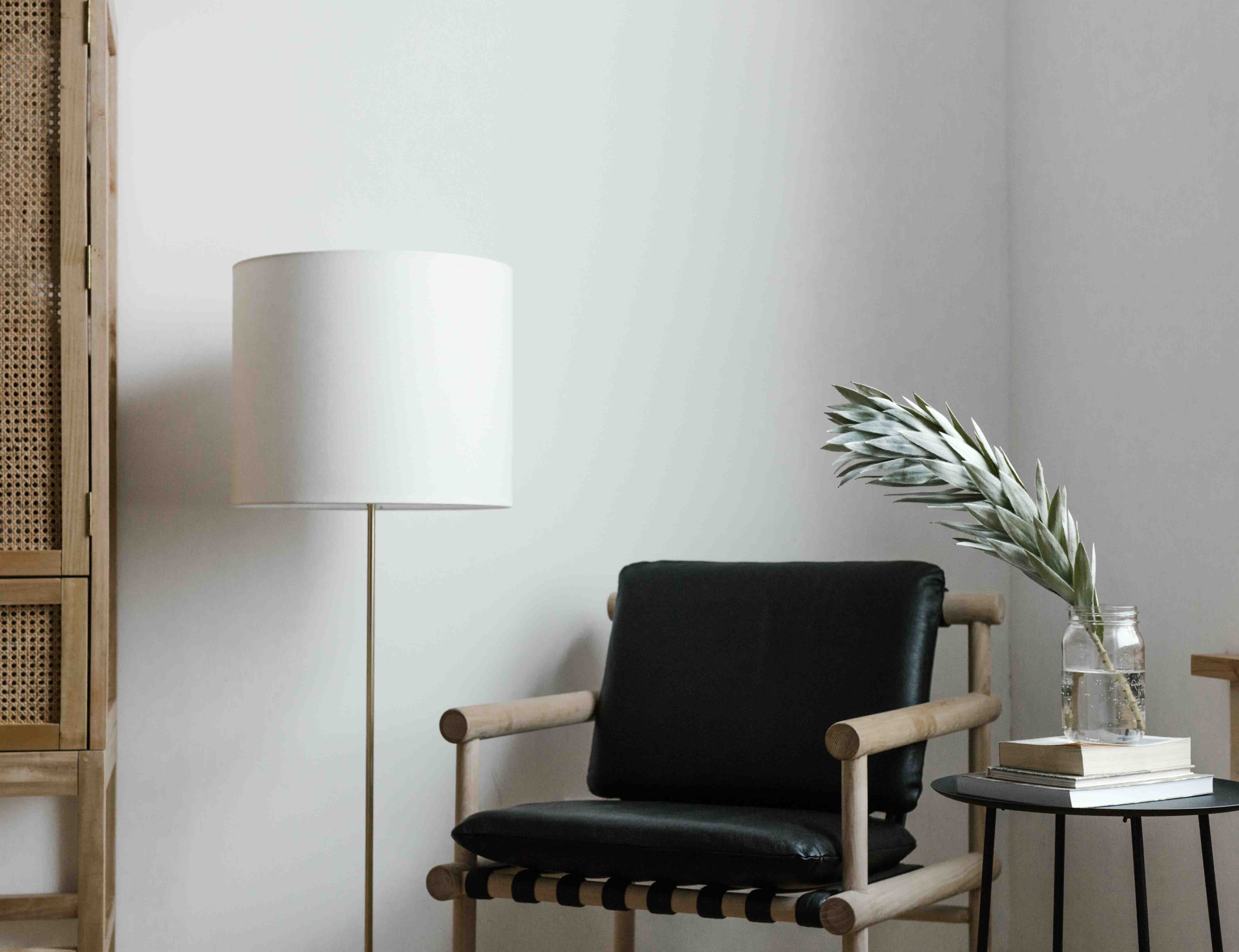 Minimalist reading nook with a black leather lounge chair, white floor lamp, and a side table holding books and a glass jar with greenery.
