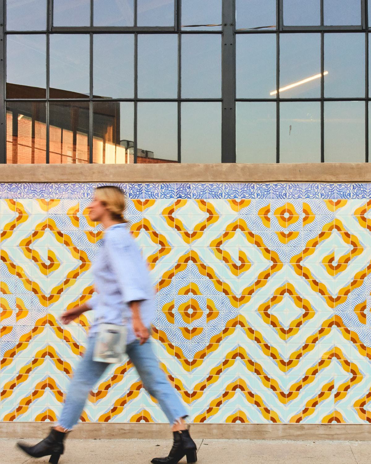person walking fast with a color la arts district mural on the wall behind them