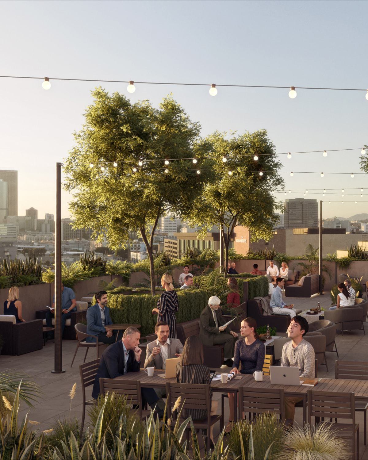 Lush rooftop workspace at Alloy LA, with people working and socializing under string lights and trees. The space features communal tables, lounge seating, and skyline views.