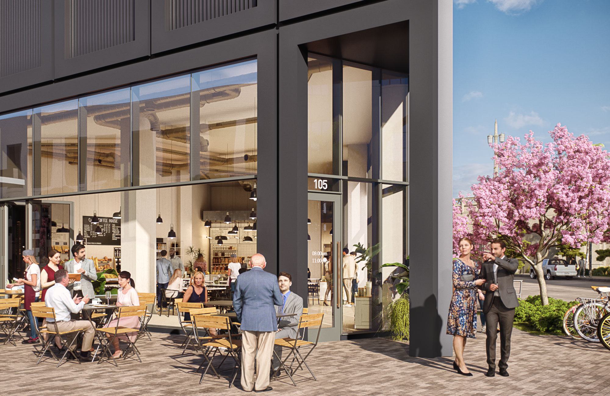 Street-level café at Alloy LA with outdoor seating, large windows, and people dining beneath a black-framed facade. A blooming pink tree and cyclists add to the lively, walkable scene.