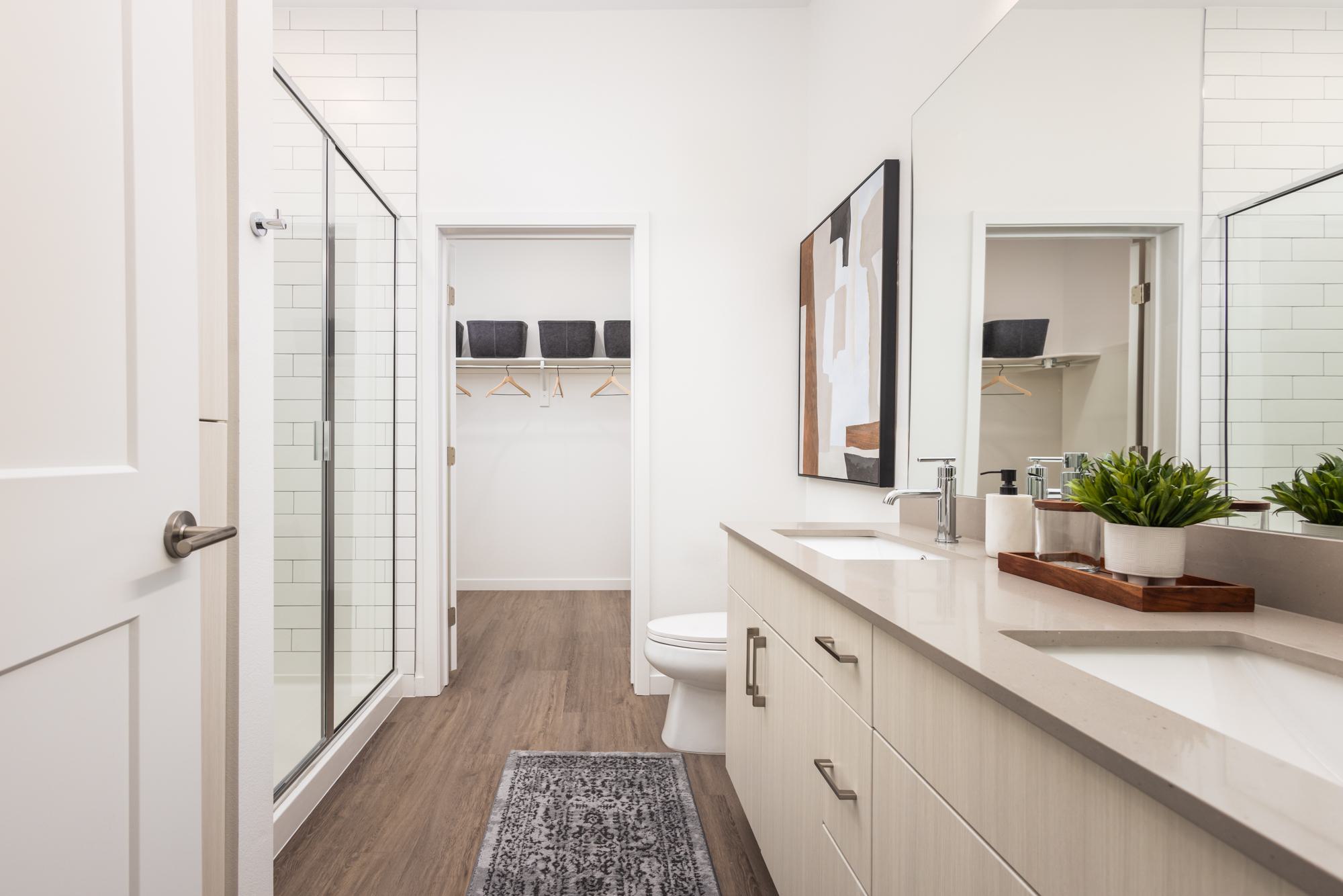 Light colored bathroom with dual sink vanity, glass enclosed shower and expansive closet