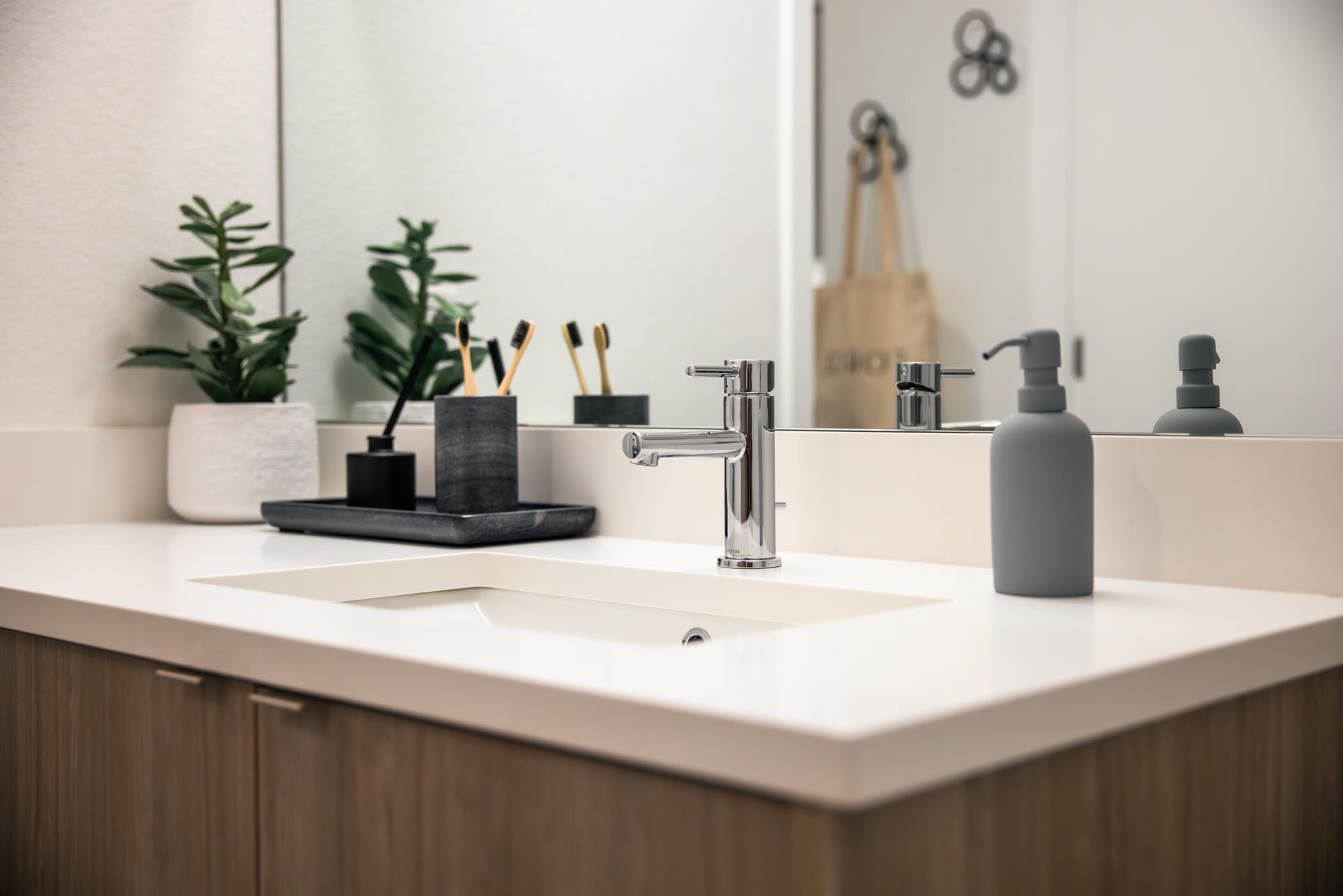Modern bathroom vanity with a chrome faucet, white quartz countertop, and minimalist accessories including a small plant and black soap tray.