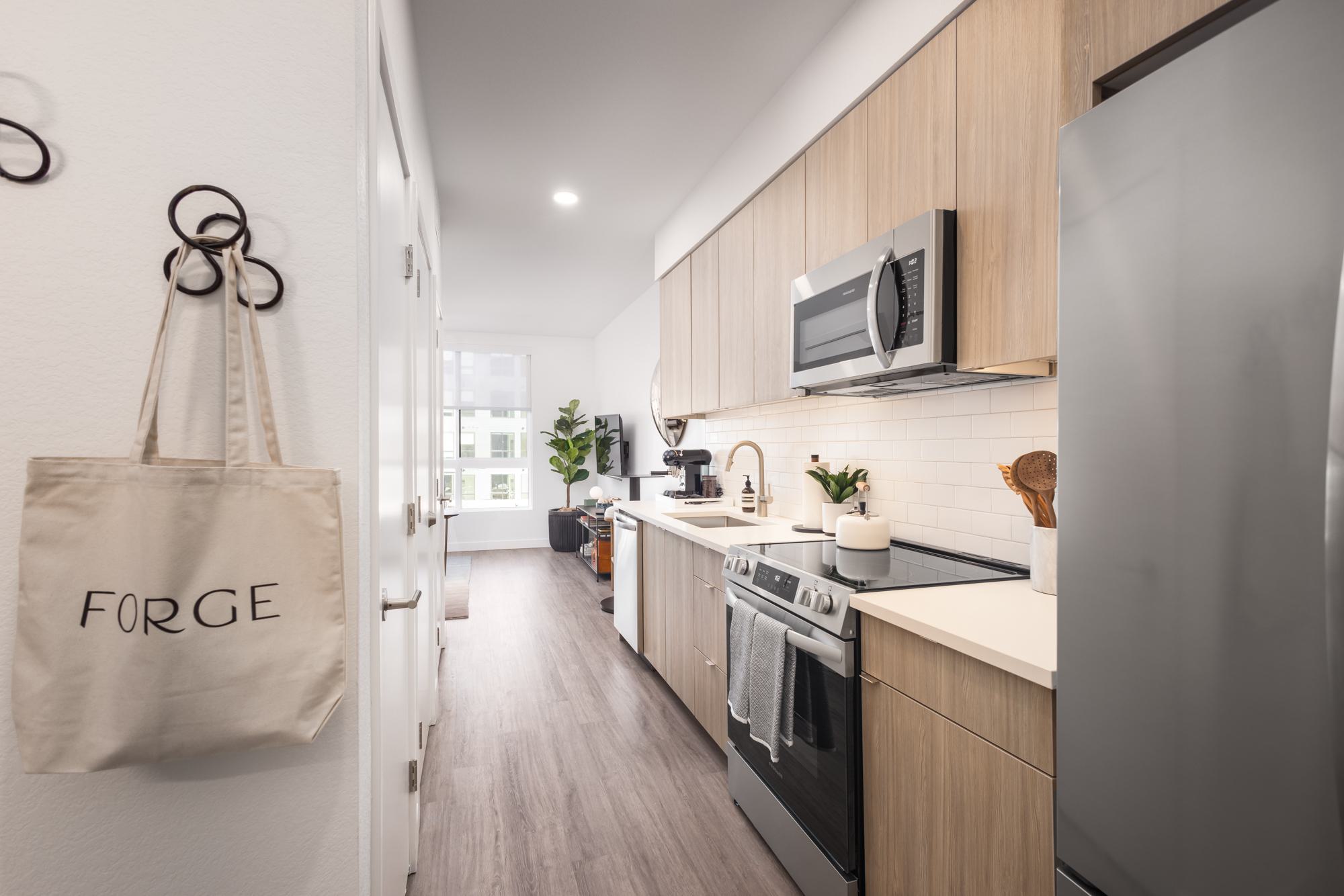 Studio apartment kitchen with wood cabinetry, stainless steel appliances, and a view into the living space.