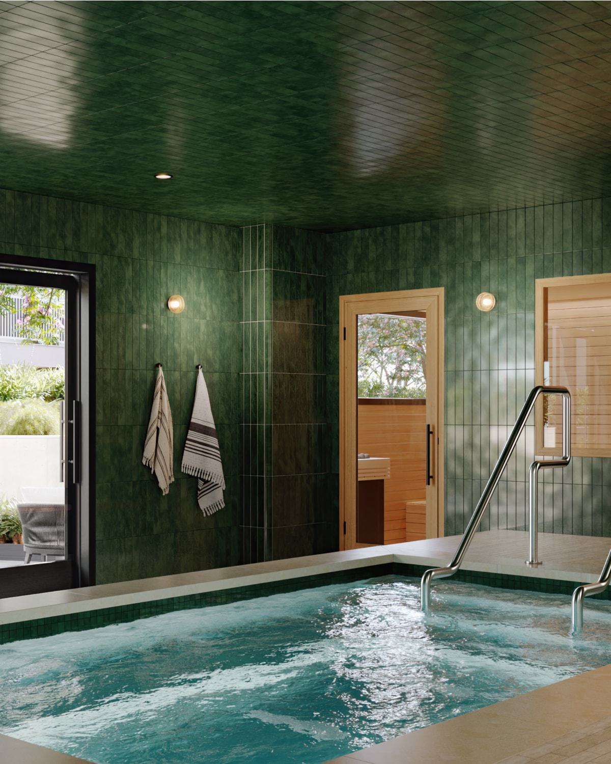 A serene indoor spa features a rectangular soaking pool framed by rich green tile walls and wood-accented sauna rooms. Floor-to-ceiling glass doors open to a tranquil outdoor lounge with blooming trees, cushioned benches, and lush landscaping.