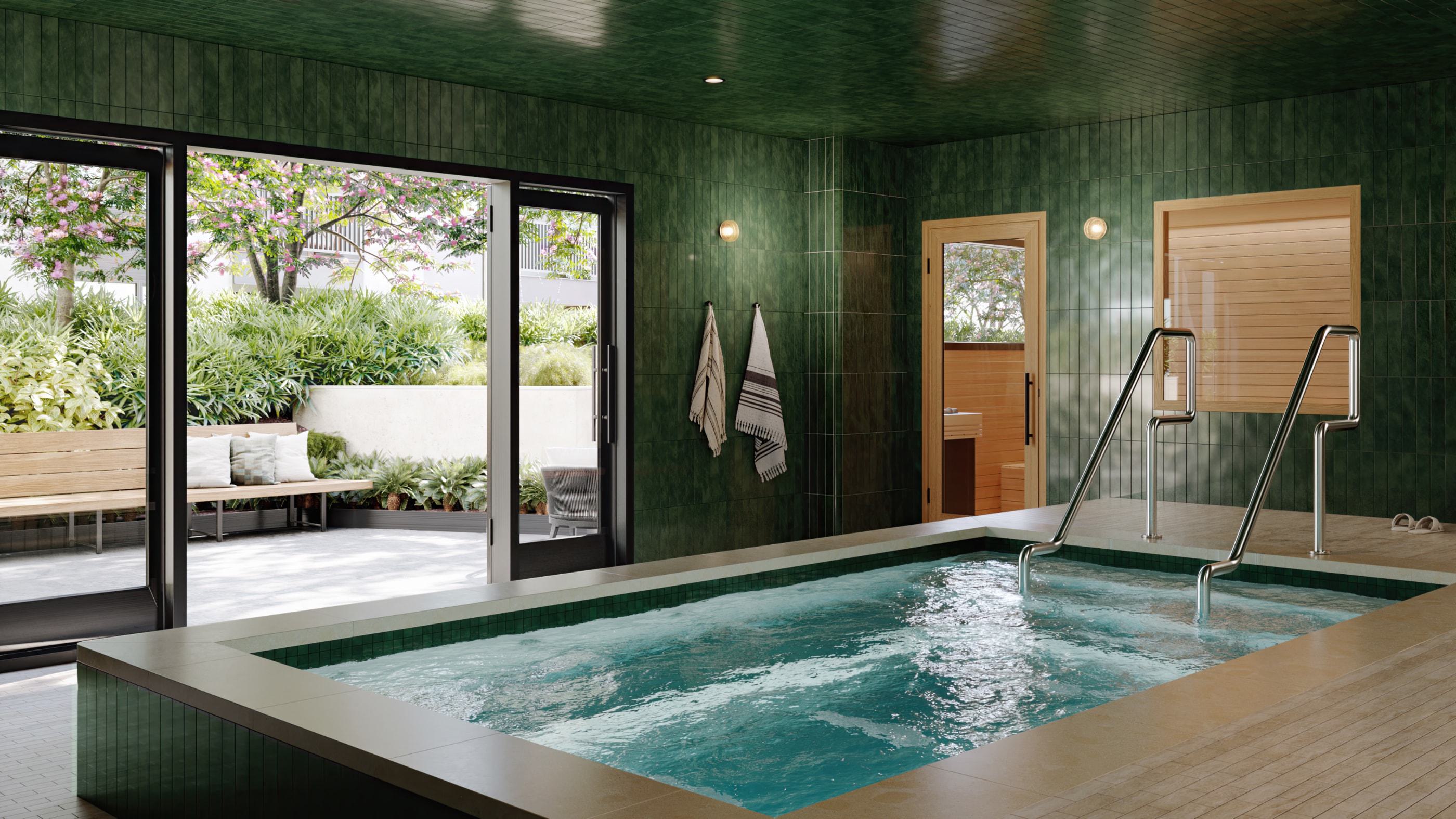 A serene indoor spa features a rectangular soaking pool framed by rich green tile walls and wood-accented sauna rooms. Floor-to-ceiling glass doors open to a tranquil outdoor lounge with blooming trees, cushioned benches, and lush landscaping.