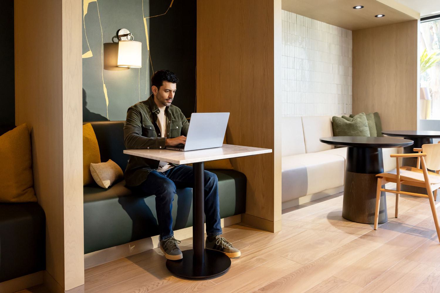 A man works on a laptop in a modern work/lounge space with wood, tile, and colorful wall accents.