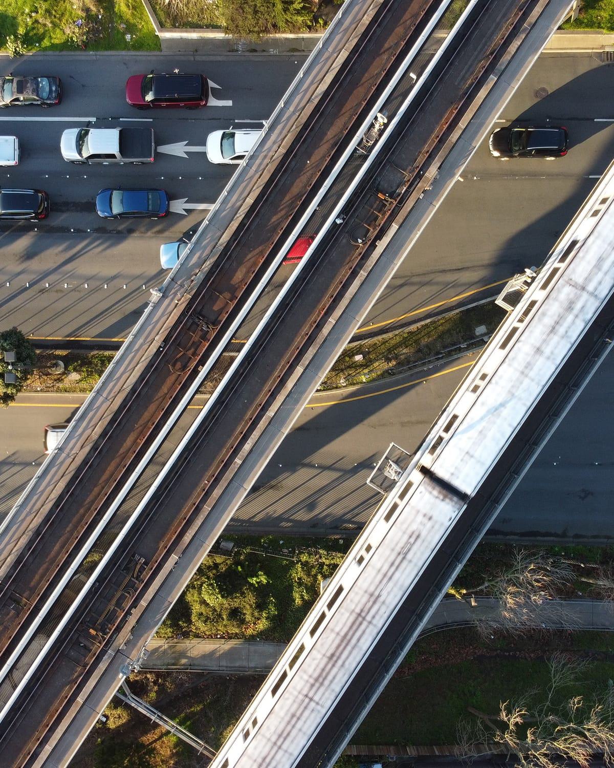 Aerial view of BART tracks running above a busy roadway with cars, showing trains and elevated rail lines crossing over lanes of traffic in Burlingame.
