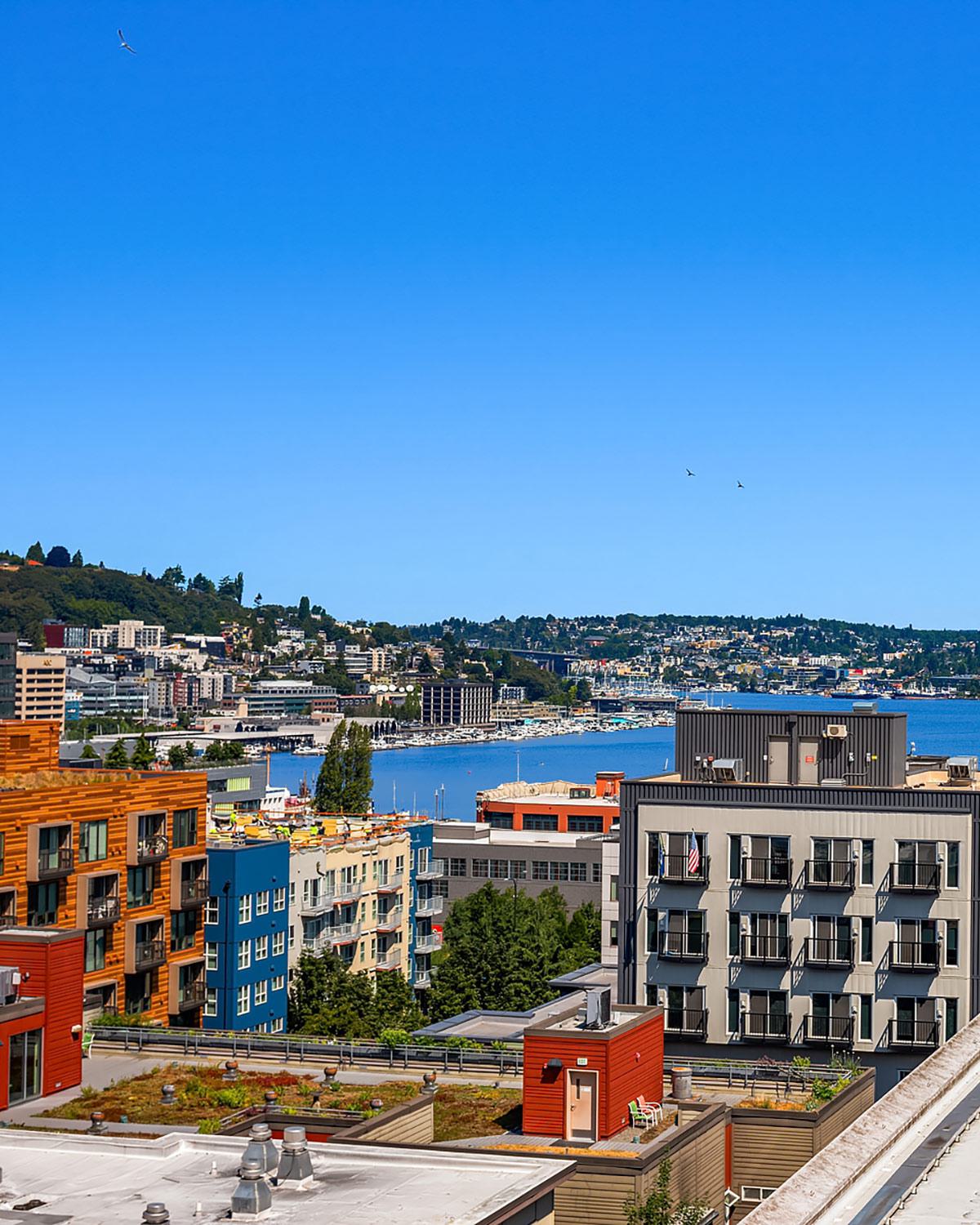 Elevated view of colorful, Chroma apartment buildings in Seattle's South Lake Union neighborhood with Lake Union and hillside homes in the background under a clear blue sky.