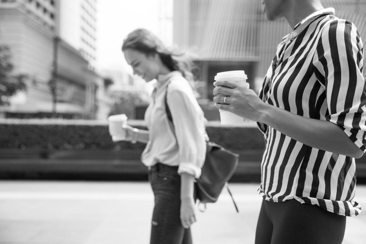 Black and white image of two women walking outside with takeaway coffee cups.