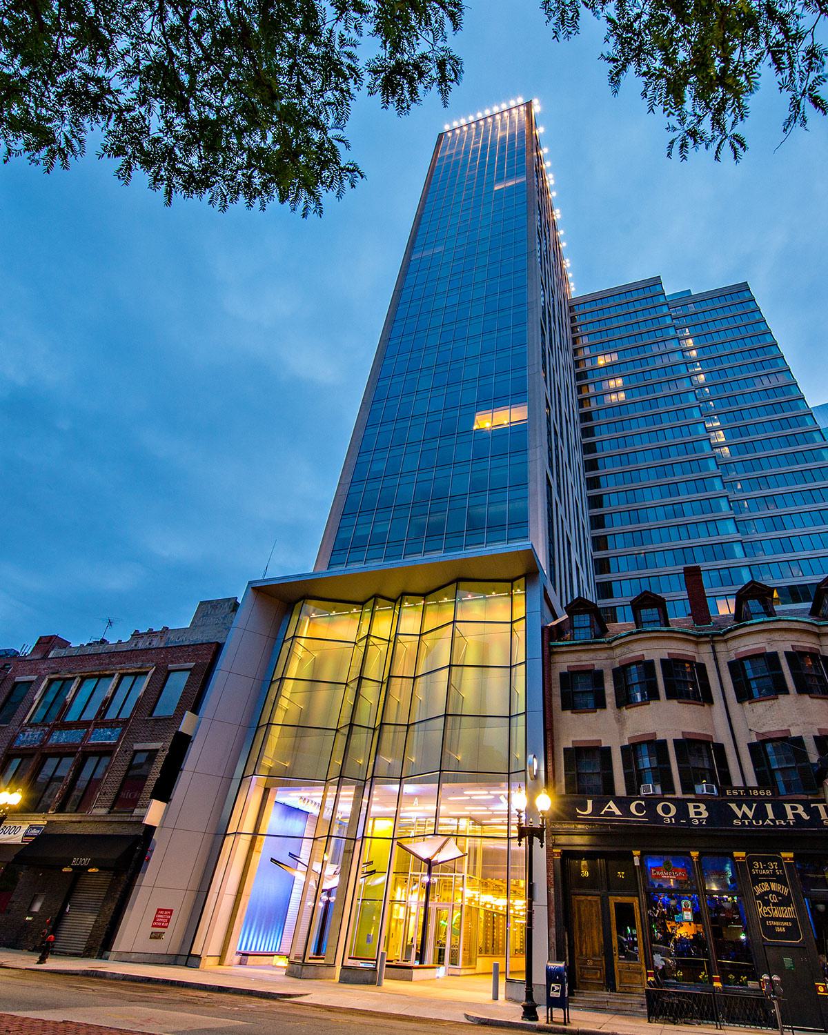 Street-level view of Luke modern glass high-rise next to historic brick buildings at dusk.