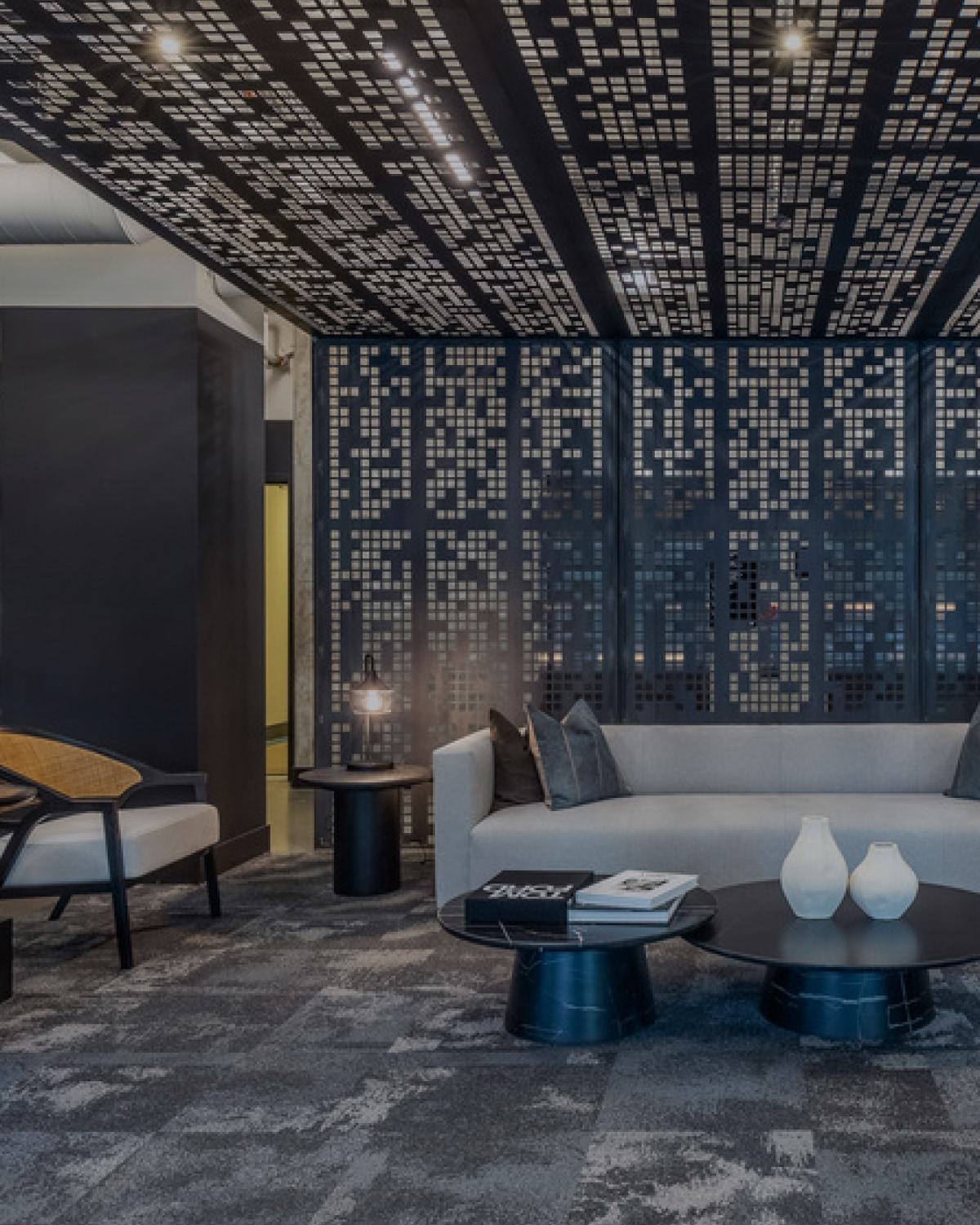 Stylish community lounge with a geometric installation on the ceiling, a couch, and several lounge chairs.