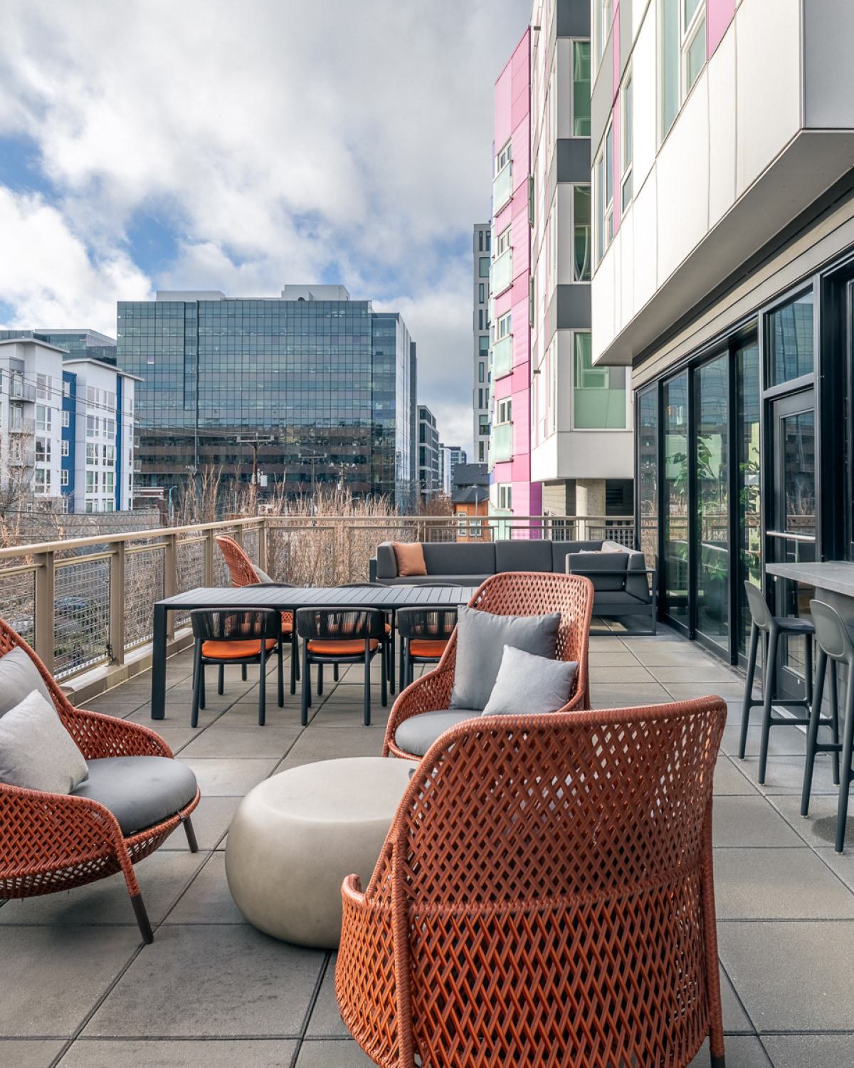 Rooftop terrace at Chroma in SLU Seattle featuring modern outdoor seating, large planters with ornamental grasses, and views of the downtown skyline under a blue sky.