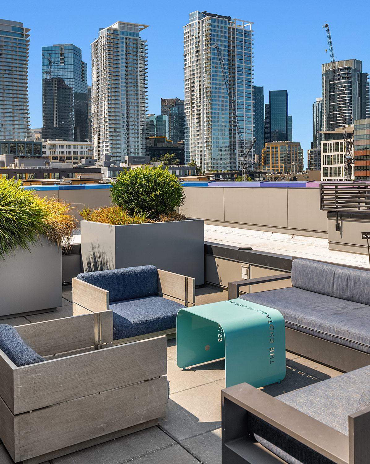Rooftop terrace at Chroma in SLU Seattle featuring modern outdoor seating, large planters with ornamental grasses, and views of the downtown skyline under a clear blue sky.