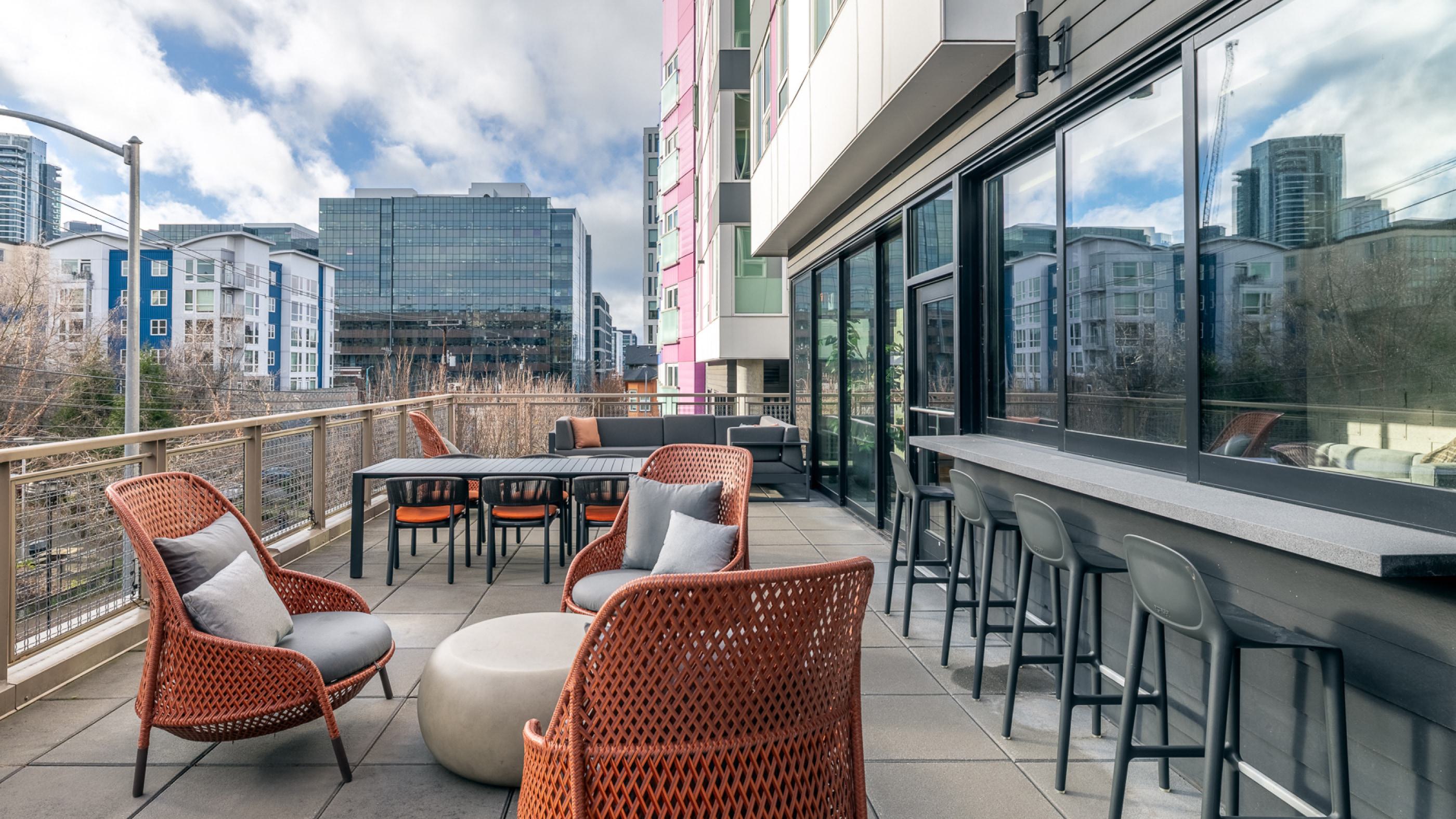 Rooftop terrace at Chroma in SLU Seattle featuring modern outdoor seating, large planters with ornamental grasses, and views of the downtown skyline under a blue sky.