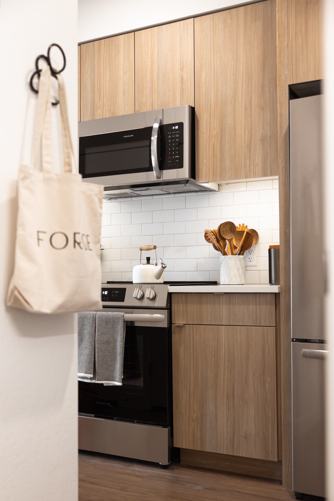 Compact kitchen with dark wood cabinets, stainless steel appliances, and white tile backsplash.