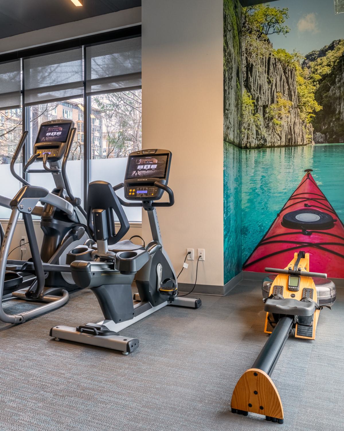 Bright, modern fitness center with floor-to-ceiling windows and a row of high-performance treadmills and elliptical machines facing the street outside.