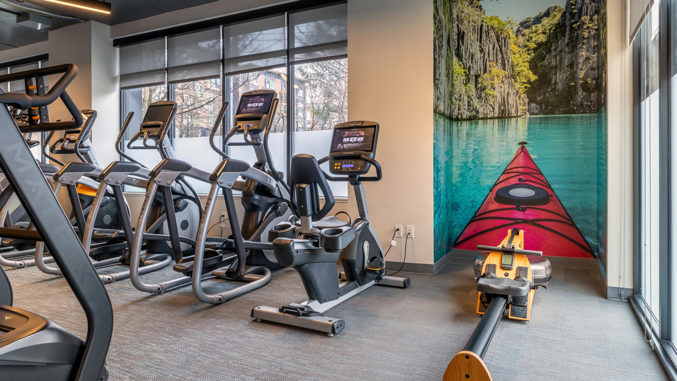 Bright, modern fitness center with floor-to-ceiling windows and a row of high-performance treadmills and elliptical machines facing the street outside.
