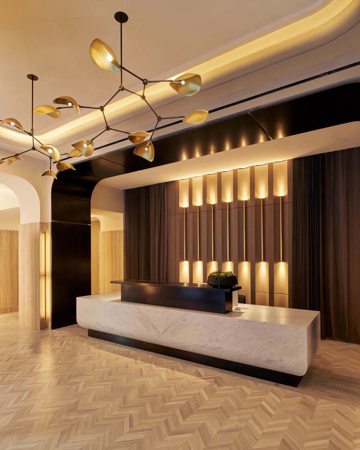 luxurious marble lobby featuring a sleek reception desk, warm wood paneling, elegant gold accents, and a sculptural chandelier, creating a sophisticated and inviting ambiance.