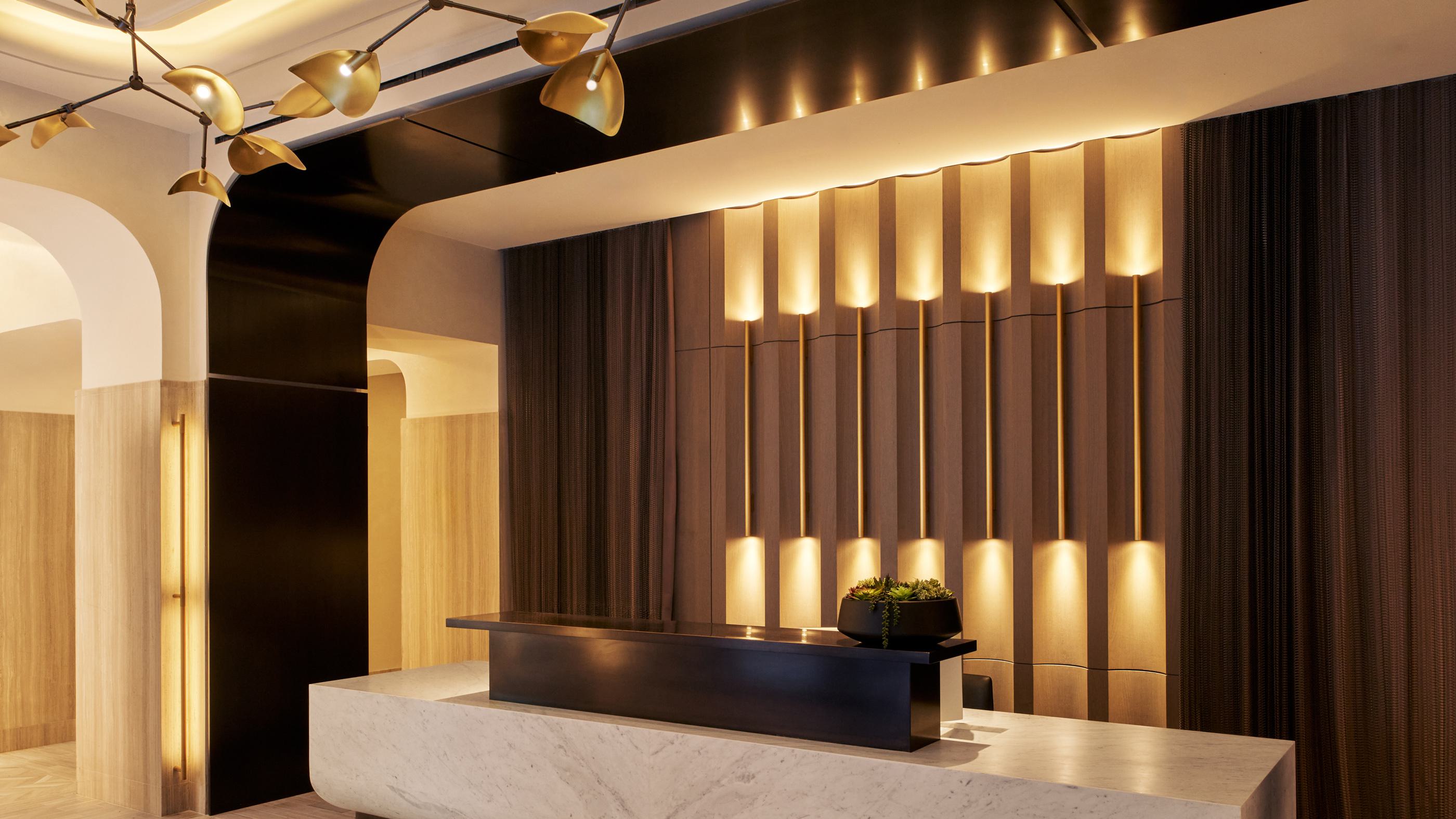 luxurious marble lobby featuring a sleek reception desk, warm wood paneling, elegant gold accents, and a sculptural chandelier, creating a sophisticated and inviting ambiance.
