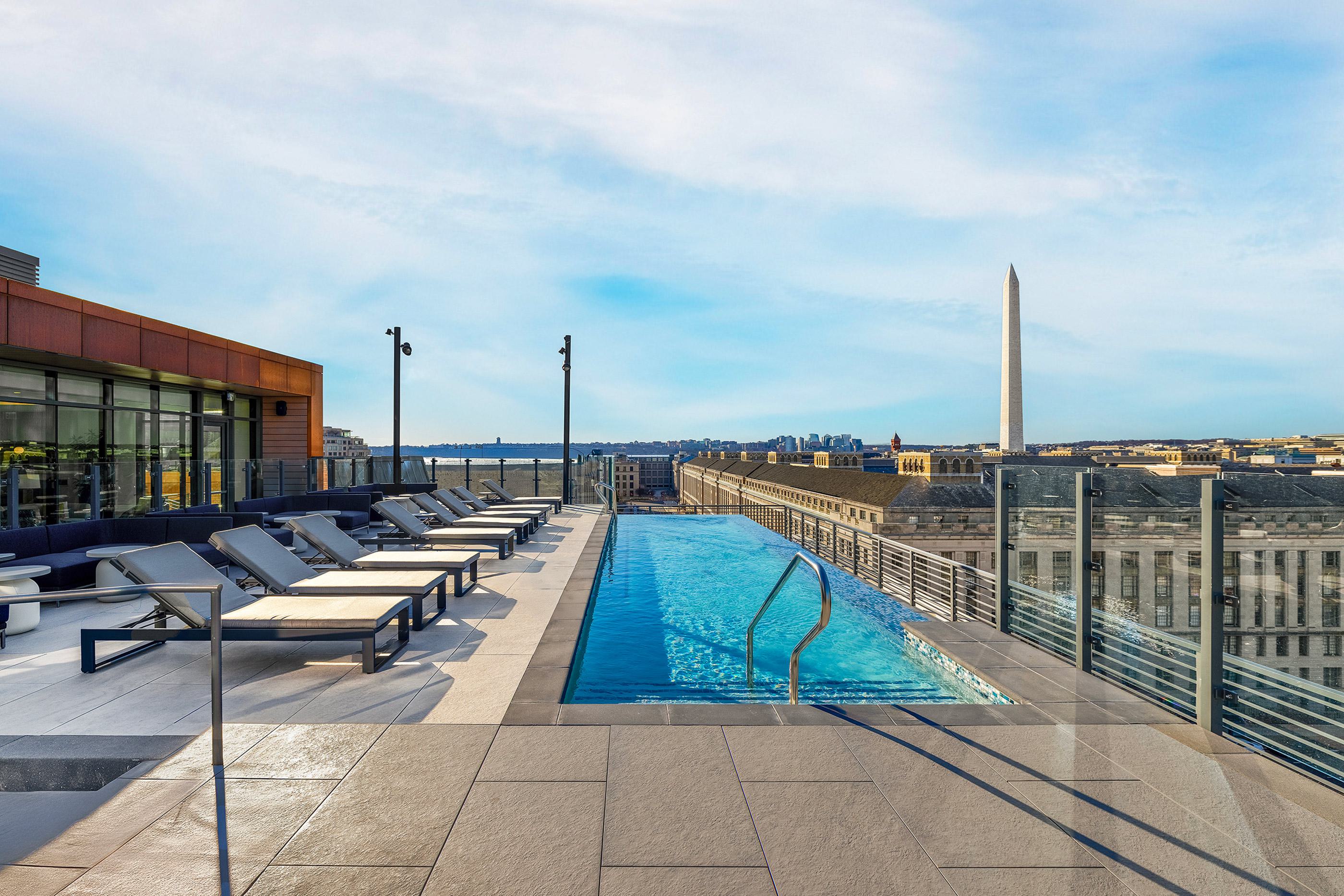 Rooftop infinity pool at DC apartment building with lounge chairs and sweeping views of the Washington Monument and city skyline.