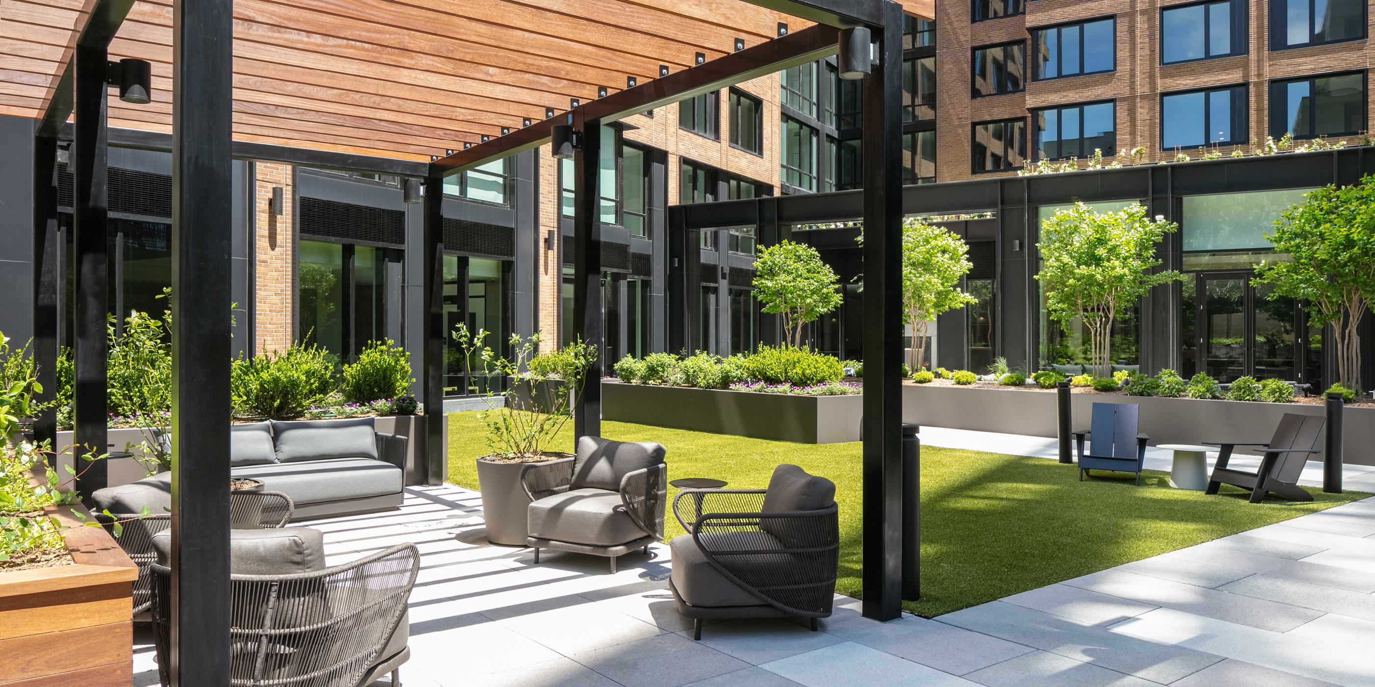 vibrant outdoor courtyard with lush greenery, shaded seating, and grilling stations, surrounded by modern apartment buildings, creating a welcoming community space.