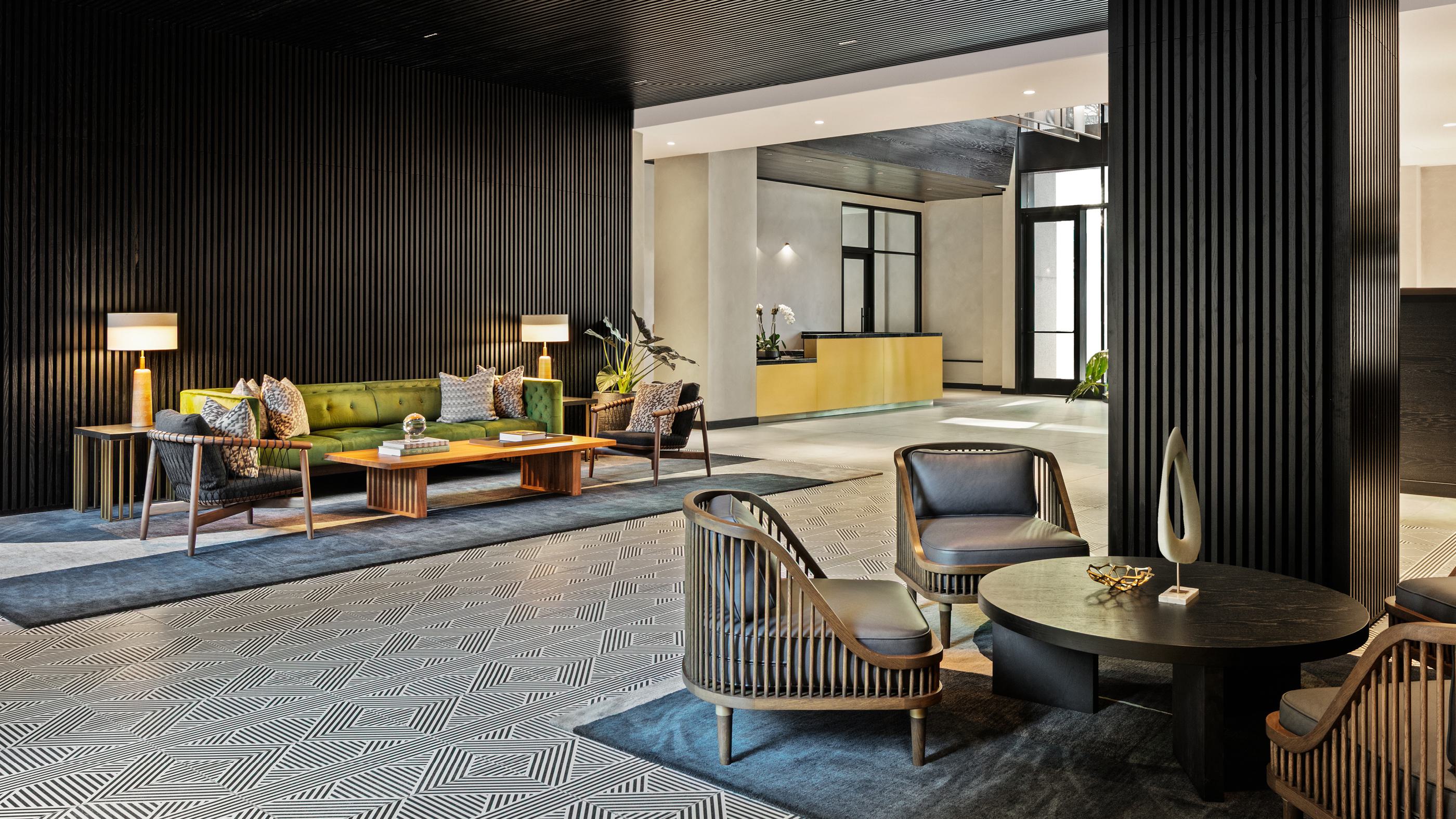 sophisticated lobby featuring a sleek gold reception desk, dark wood ceiling accents, and a seamless transition to a lush courtyard lounge.