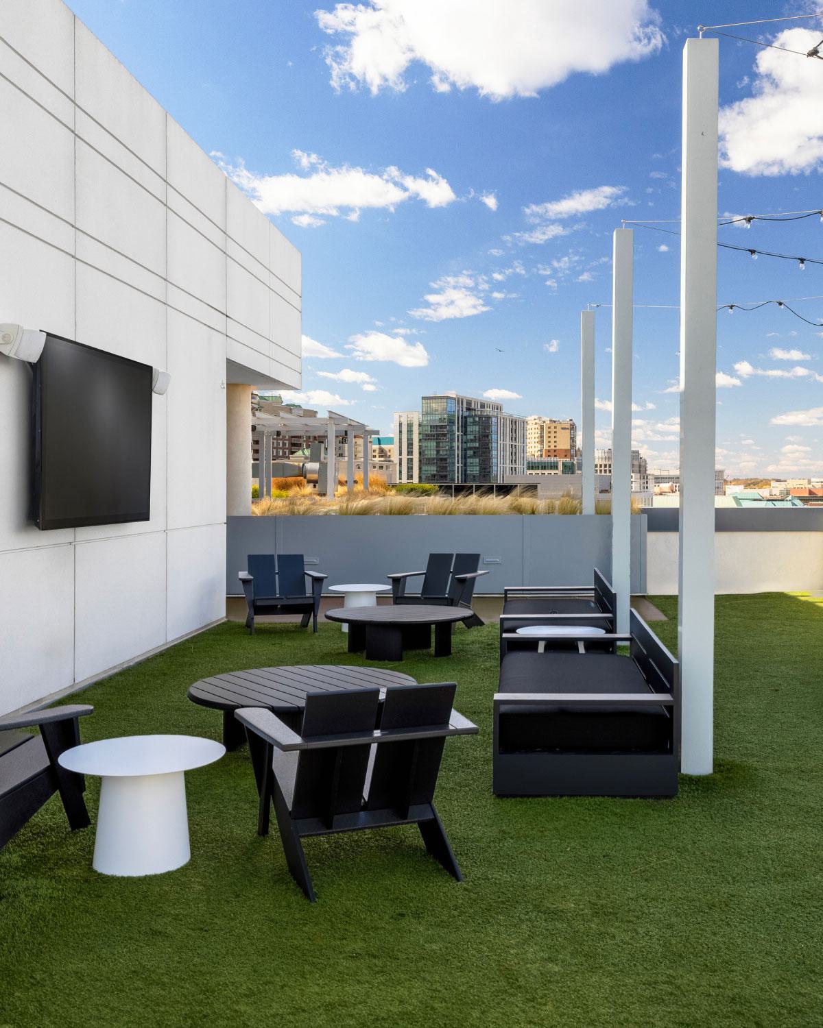 Rooftop social lawn at Latitude Apartments in Virginia Square with turf seating, outdoor lounge furniture, string lighting, yard games, and elevated views across Arlington’s tree-lined neighborhoods.