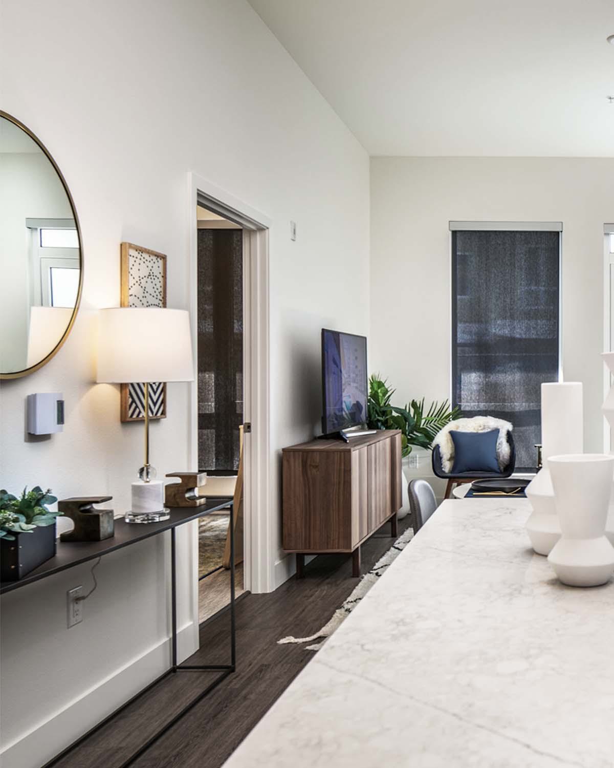 Bright, open-concept apartment interior at Latitude Apartments in Arlington, VA, featuring a modern kitchen with stone waterfall island, stainless steel appliances, contemporary cabinetry, and a living area with large windows and curated furnishings.