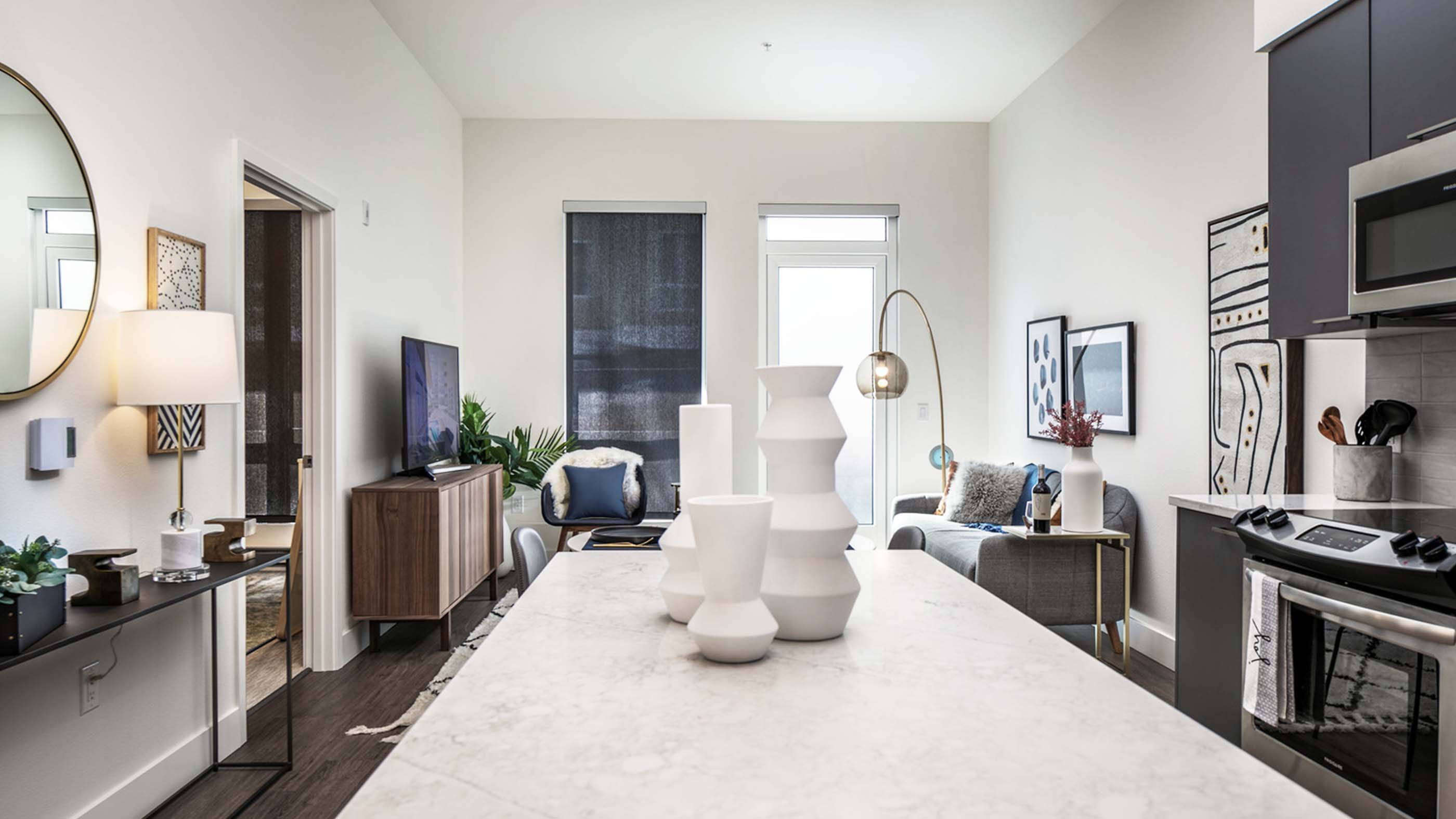 Bright, open-concept apartment interior at Latitude Apartments in Arlington, VA, featuring a modern kitchen with stone waterfall island, stainless steel appliances, contemporary cabinetry, and a living area with large windows and curated furnishings.