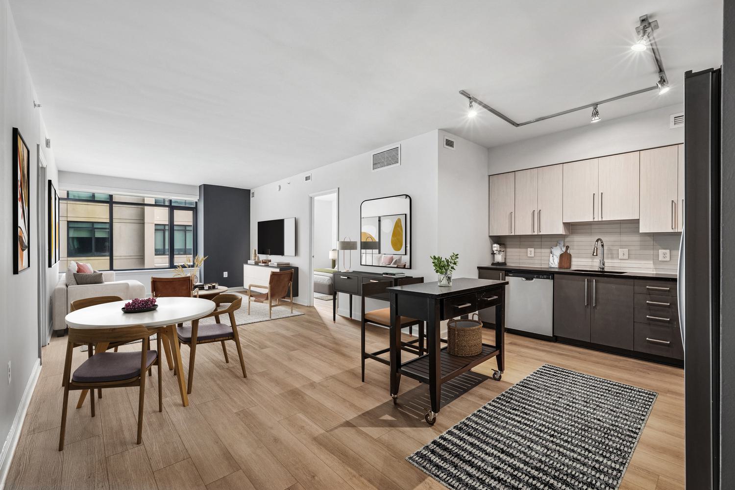 Close-up of a modern apartment kitchen island at Latitude Apartments in Arlington, VA, featuring a polished chrome gooseneck faucet set into a smooth stone countertop, with stainless steel refrigerator and minimalist cabinetry in the background.