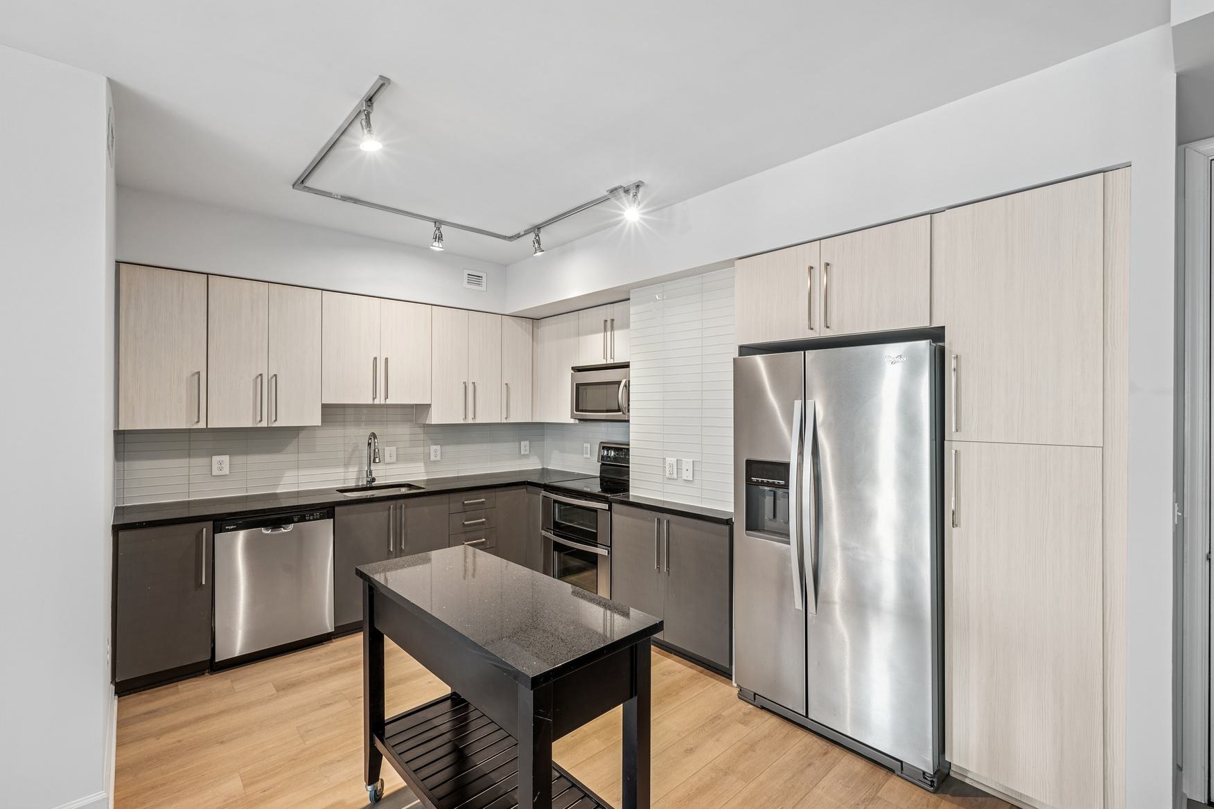 Close-up of a styled apartment kitchen sink at Latitude Apartments in Arlington, VA, featuring a chrome gooseneck faucet, integrated undermount sink, minimalist countertop accessories, and cocktail glasses arranged on a wood tray, with soft natural light in the background.