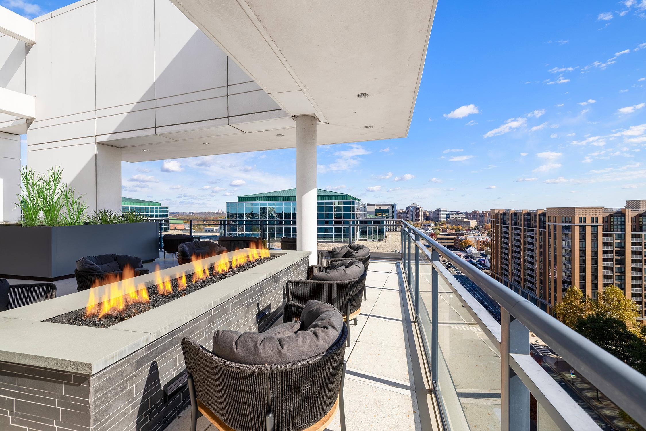 Rooftop terrace at Latitude Apartments in Virginia Square with a modern linear fire pit, cushioned lounge seating, glass railings, and expansive Arlington skyline views.