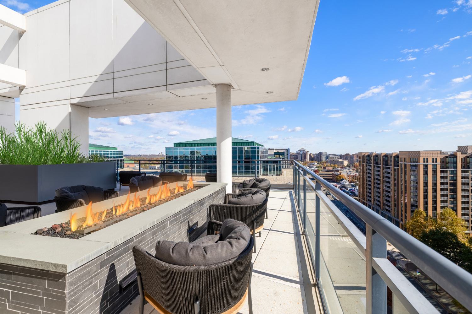Rooftop terrace at Latitude Apartments in Virginia Square with a modern linear fire pit, cushioned lounge seating, glass railings, and expansive Arlington skyline views.